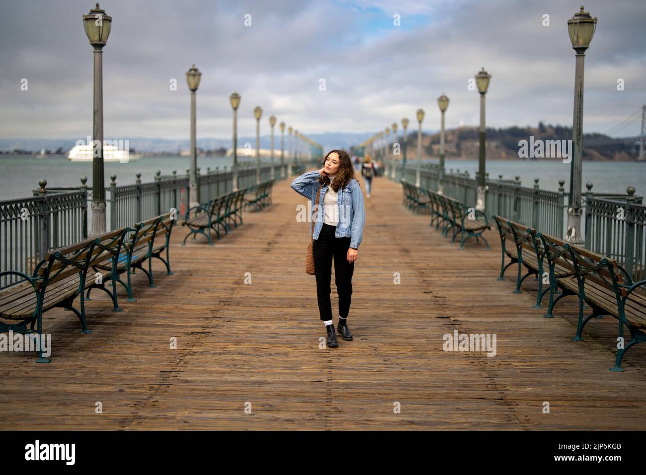 Unposed Portrait of Young Woman on Pier 7 Walking Towards Camera with San Francisco Bay in the Background Stock Photo