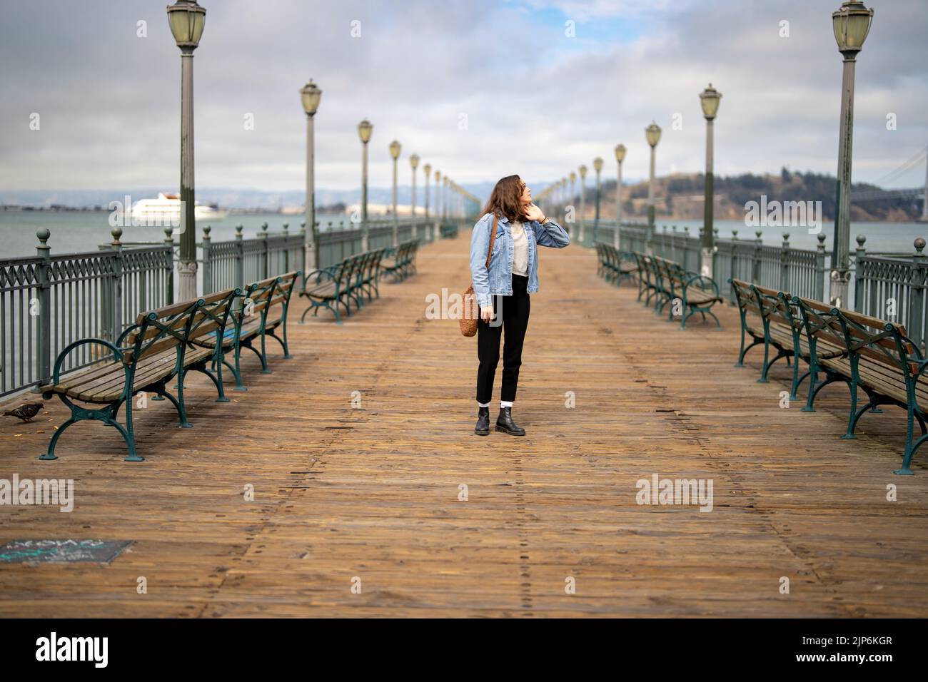 Unposed Portrait of Young Woman on Pier 7 Walking Towards Camera with San Francisco Bay in the Background Stock Photo