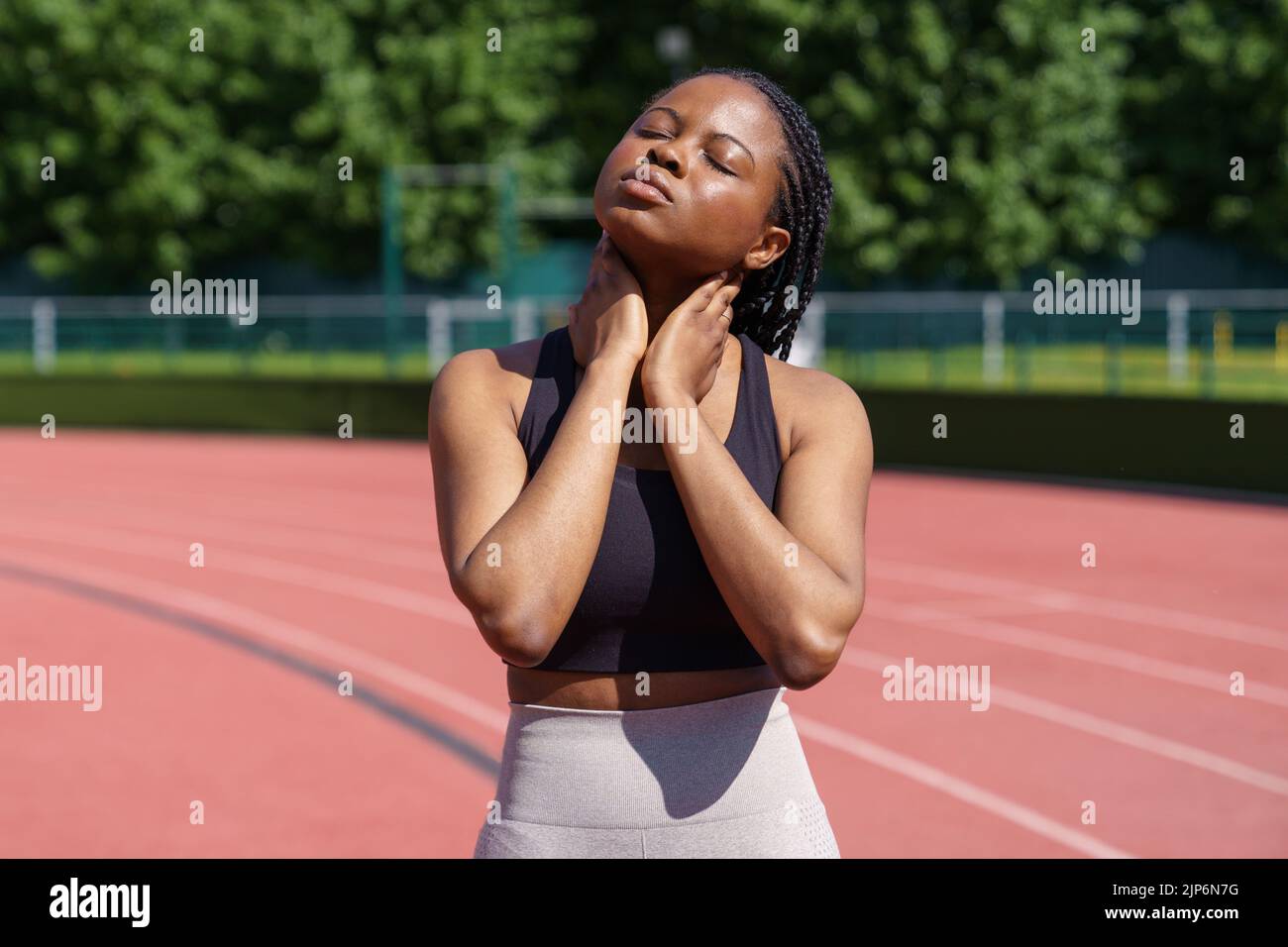 Sportive African American woman puts hands on stiff neck leaning head to sides on blurred