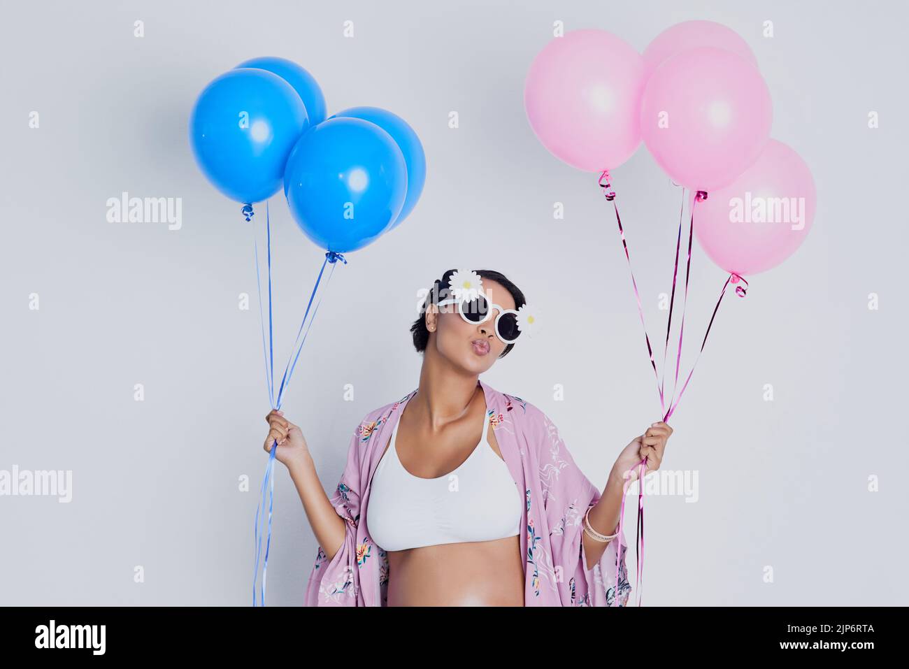 Will it be a girl or a boy. Studio shot of a beautiful young pregnant woman holding blue and pink balloons against a gray background. Stock Photo