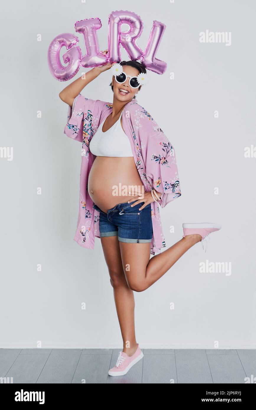 Its a girl. Studio shot of a beautiful young pregnant woman holding up a word balloon that reads girl against a gray background. Stock Photo