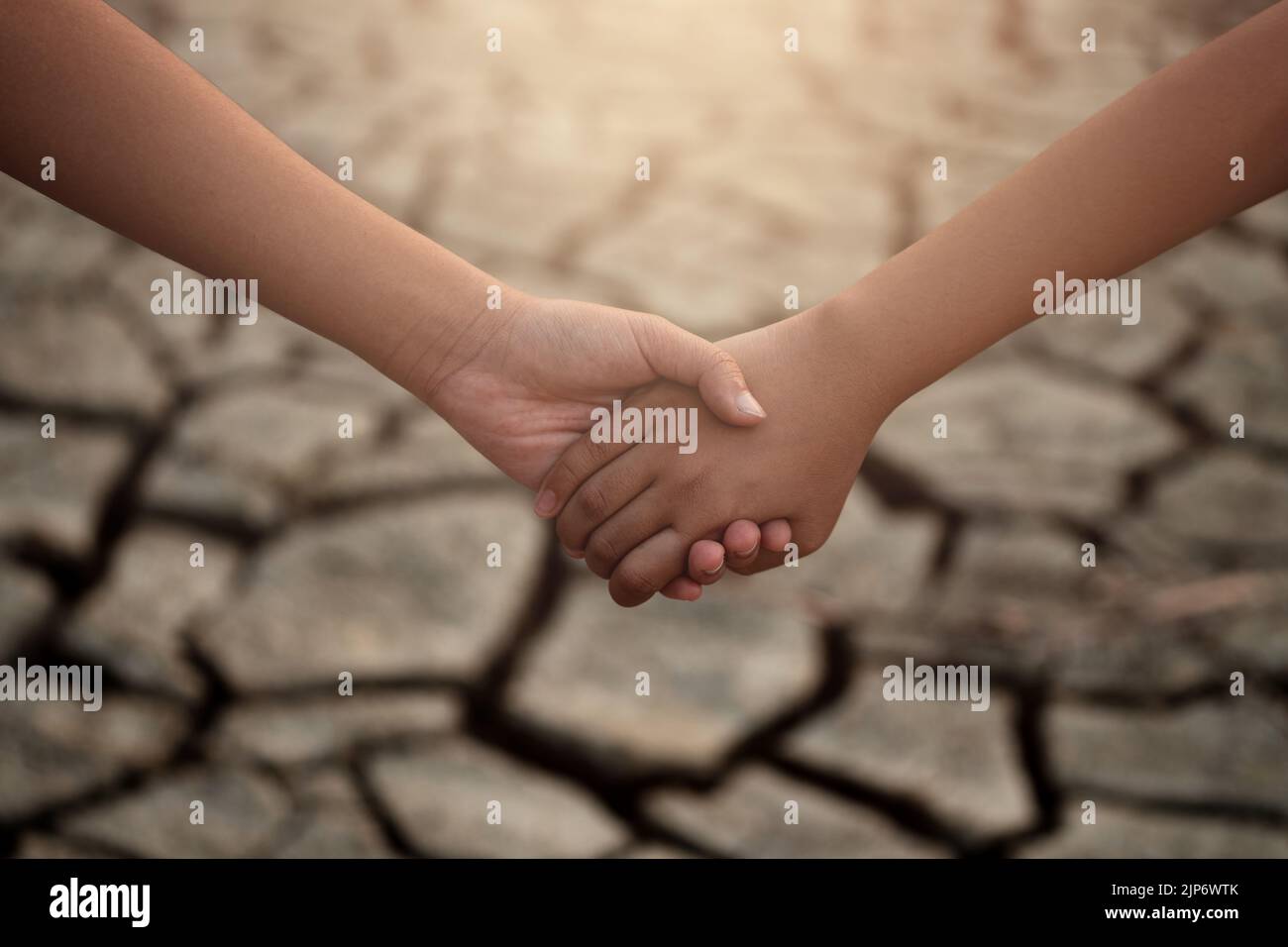 Young boy and girl holding hands on cracks in the dried soil in arid season. Saving environment and natural conservation concept. Stock Photo