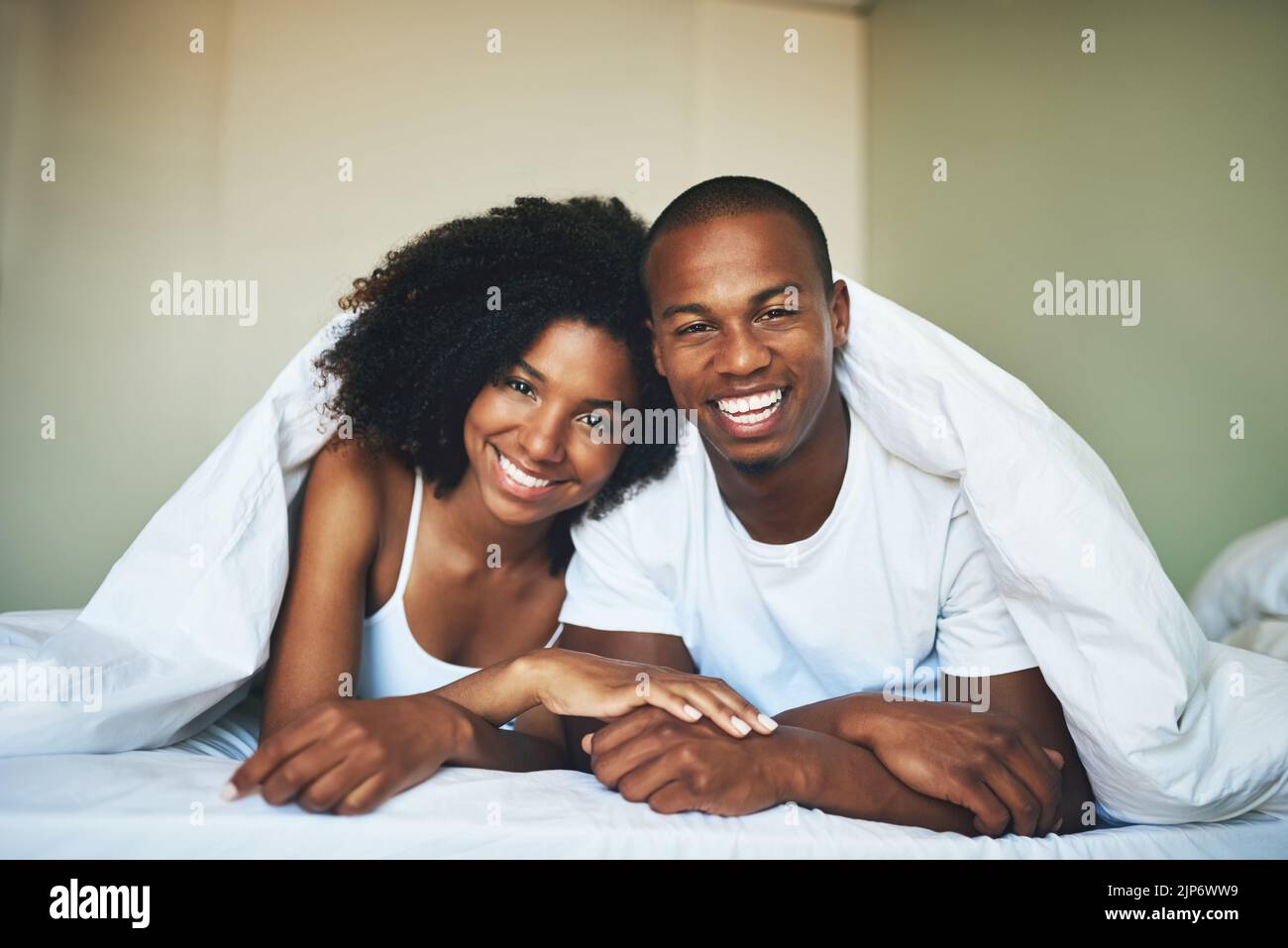 This is how we do weekends. Portrait of a happy young couple relaxing under a duvet in their bedroom. Stock Photo