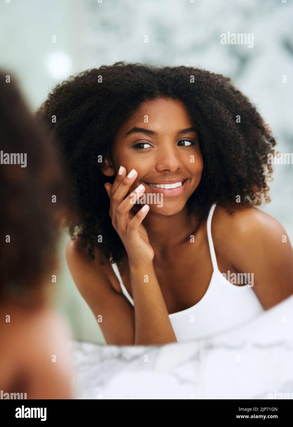 My skin has cleared up so beautifully. an attractive young woman looking at her face in the mirror at home. Stock Photo