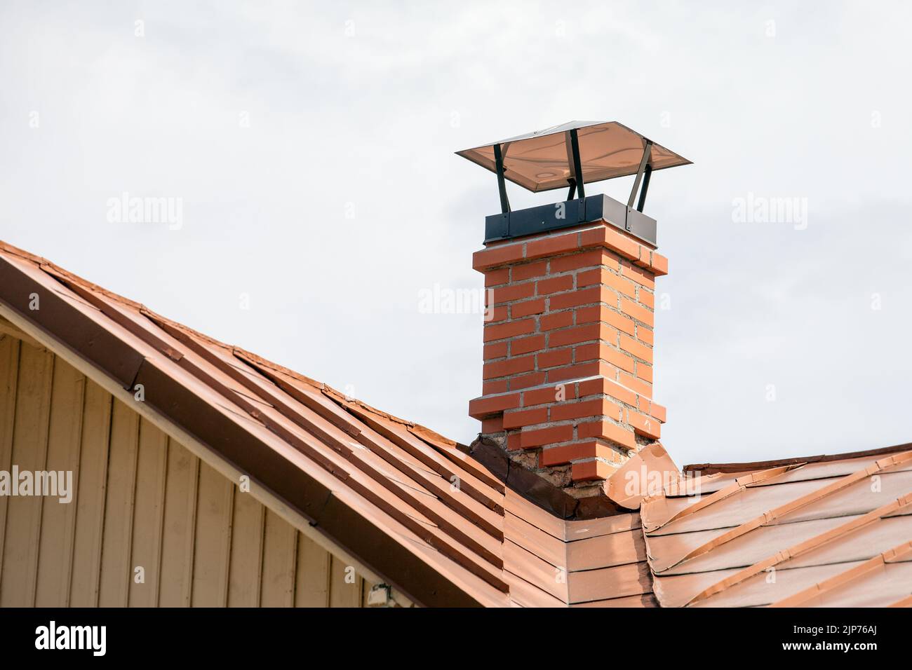 Red brick chimney with a metal roof. Stock Photo