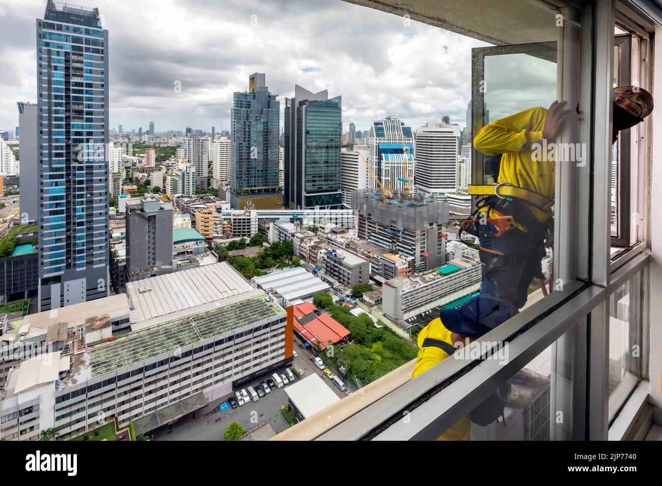 Thai workers repairing windows on high rise skyscraper above Bangkok, Thailand Stock Photo