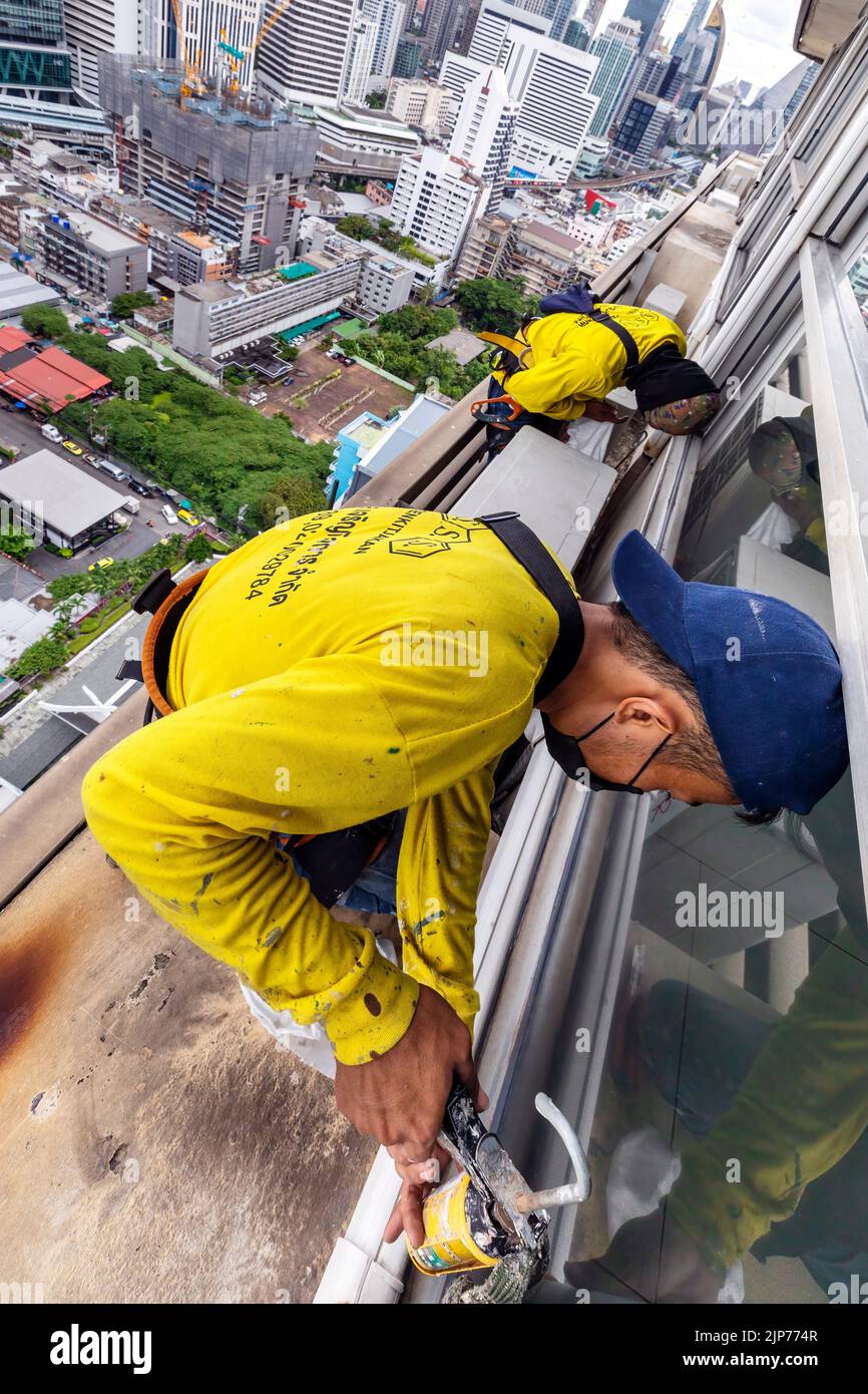 Thai workers repairing windows on high rise skyscraper above Bangkok, Thailand Stock Photo