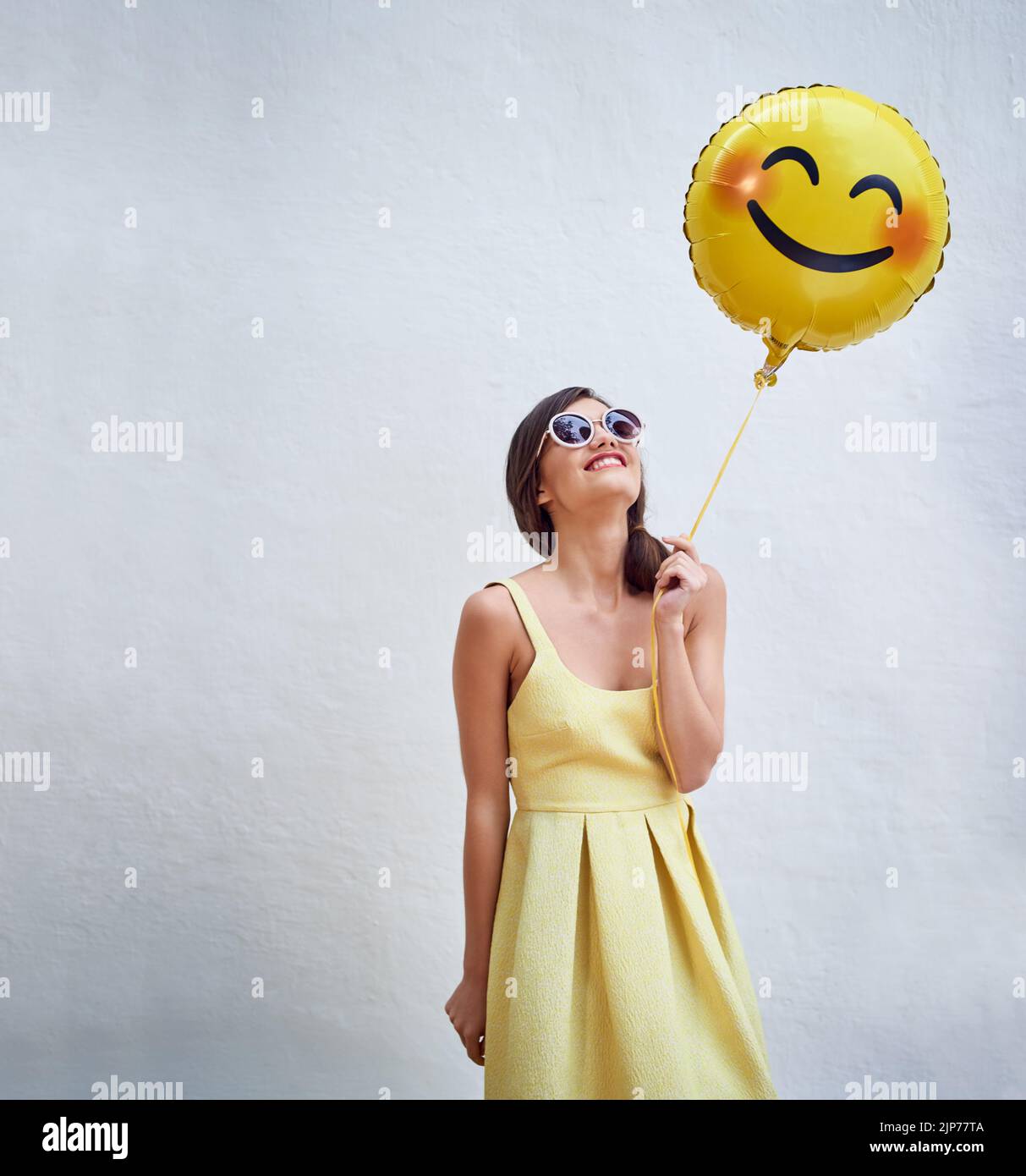 Stay happy. Studio shot of a cheerful young woman holding a smiling emoticon balloon while standing against a grey background. Stock Photo