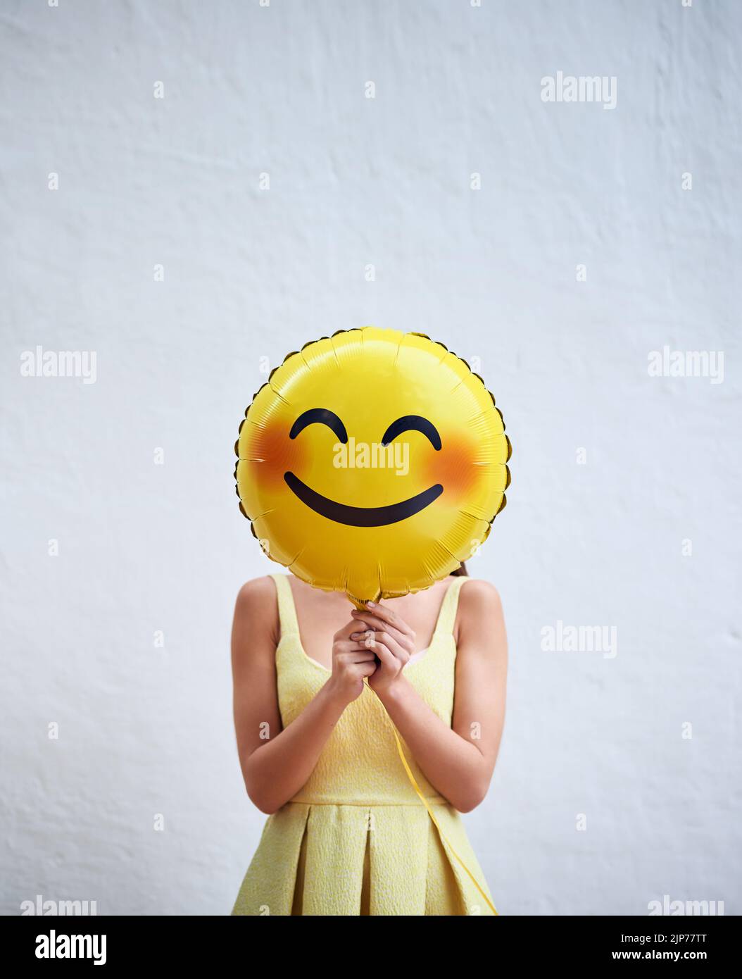 Keep smiling. Studio shot of an unrecognizable woman holding a smiling emoticon balloon in front of her face against a grey background. Stock Photo