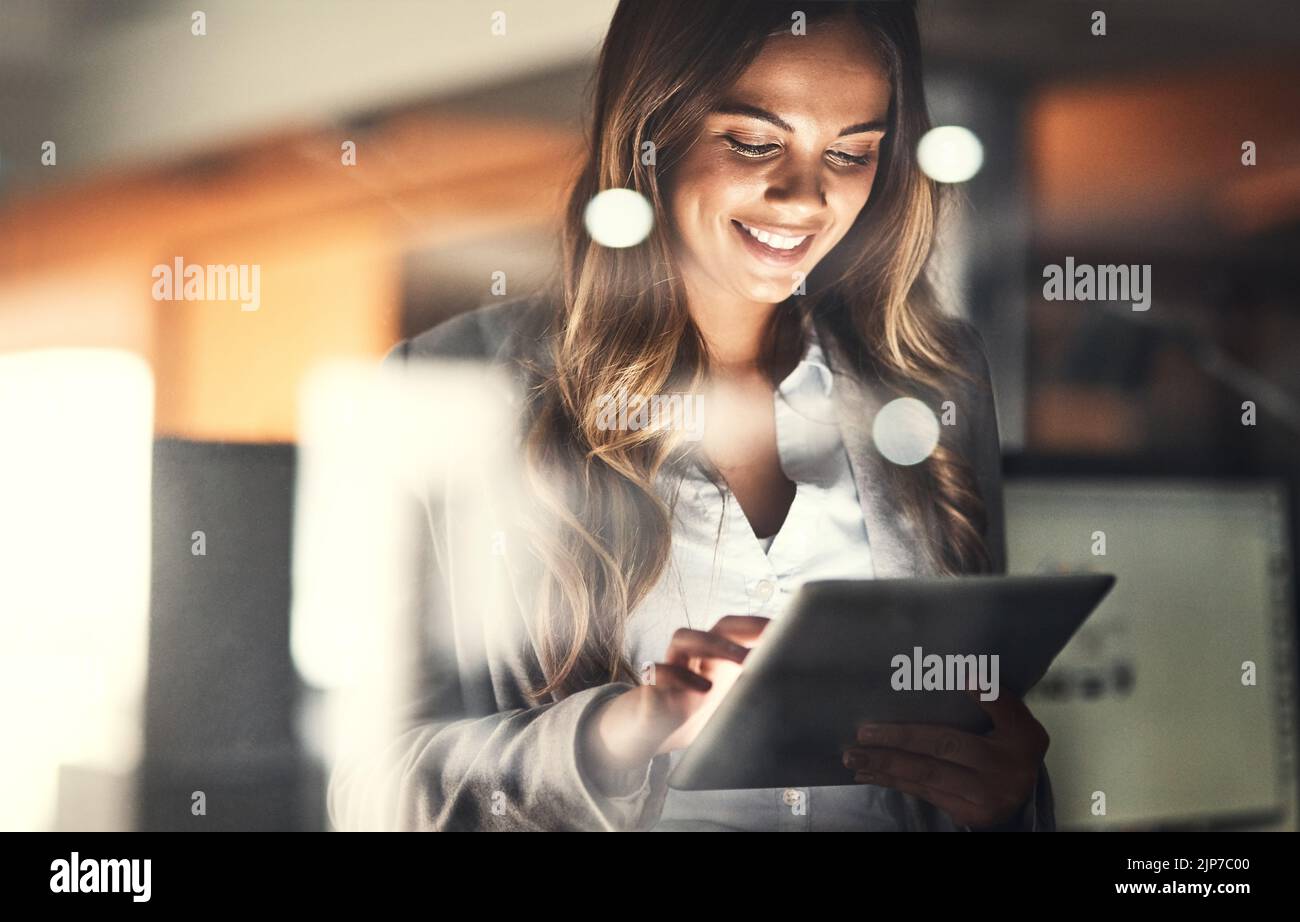Working late, overtime and dedication with a happy, positive and motivated business woman working on a tablet in her office. Young female executive Stock Photo