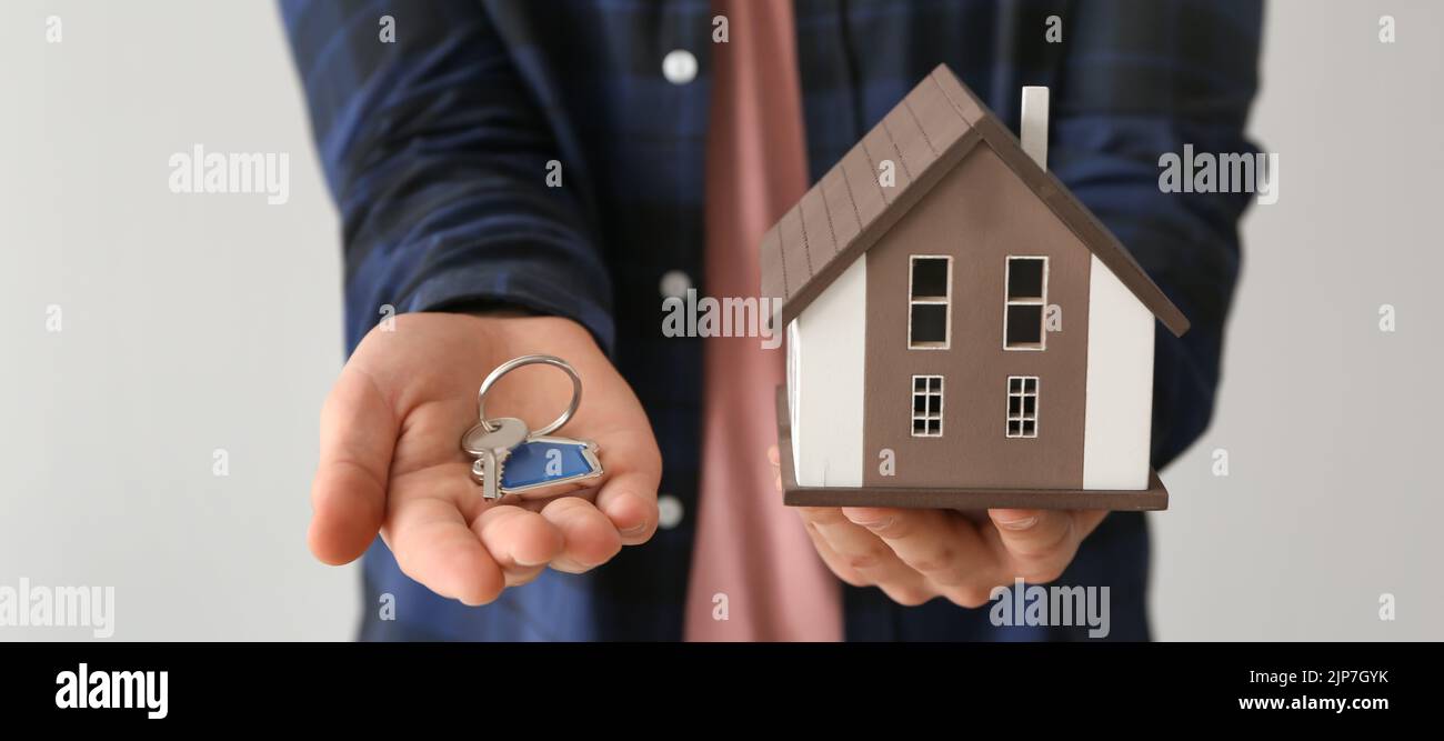 Real estate agent holding house model and key on light background ...