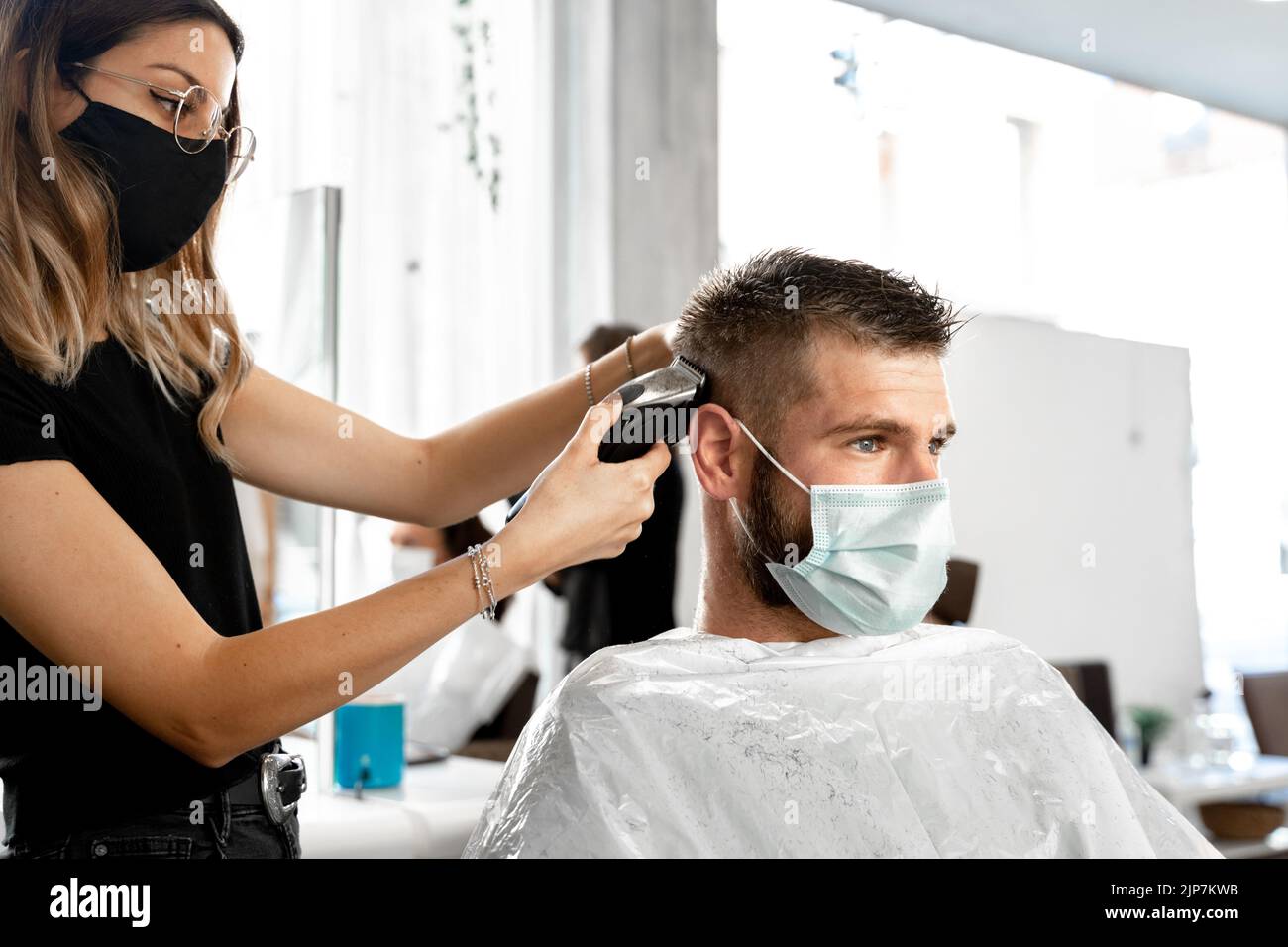 Hairdresser trimming the hair of a client with facial mask in a beauty salon Stock Photo Alamy