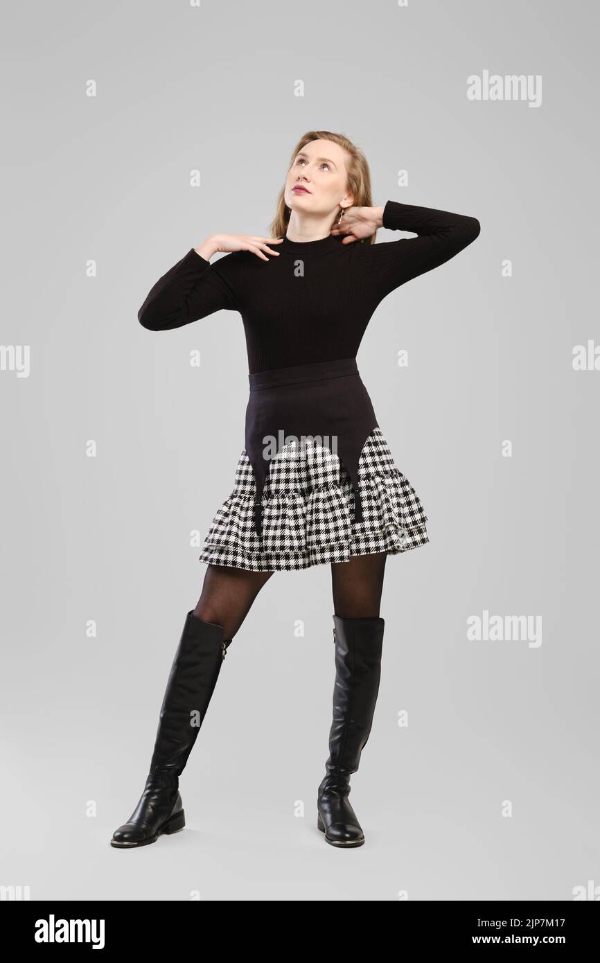 Full length portrait of young woman in turtleneck and suspender belt over little skirt posing in studio over grey background Stock Photo