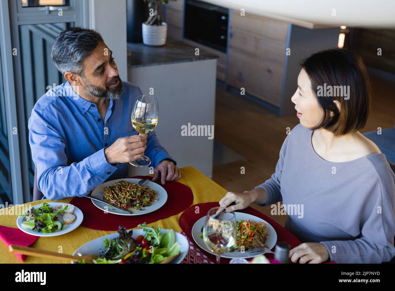 Happy diverse couple sitting at table, eating dinner together Stock Photo