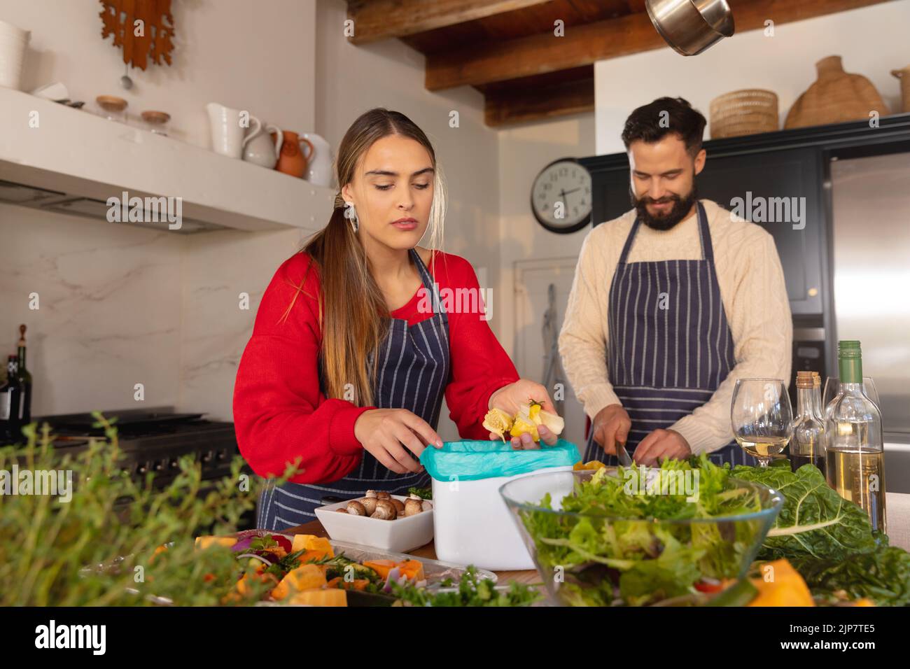 Happy caucasian couple preparing food in kitchen and composting vegetable scraps Stock Photo