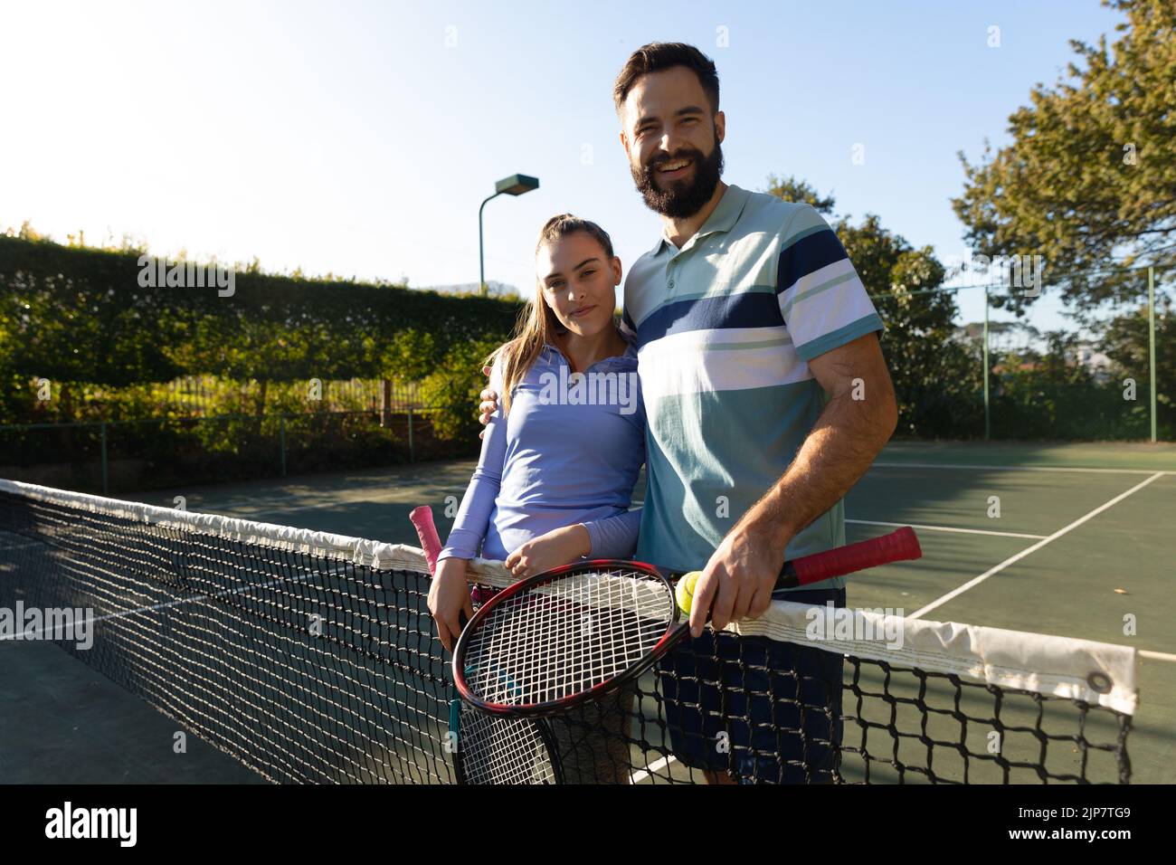 Image of happy caucasian couple posing with rackets on tennis court Stock Photo