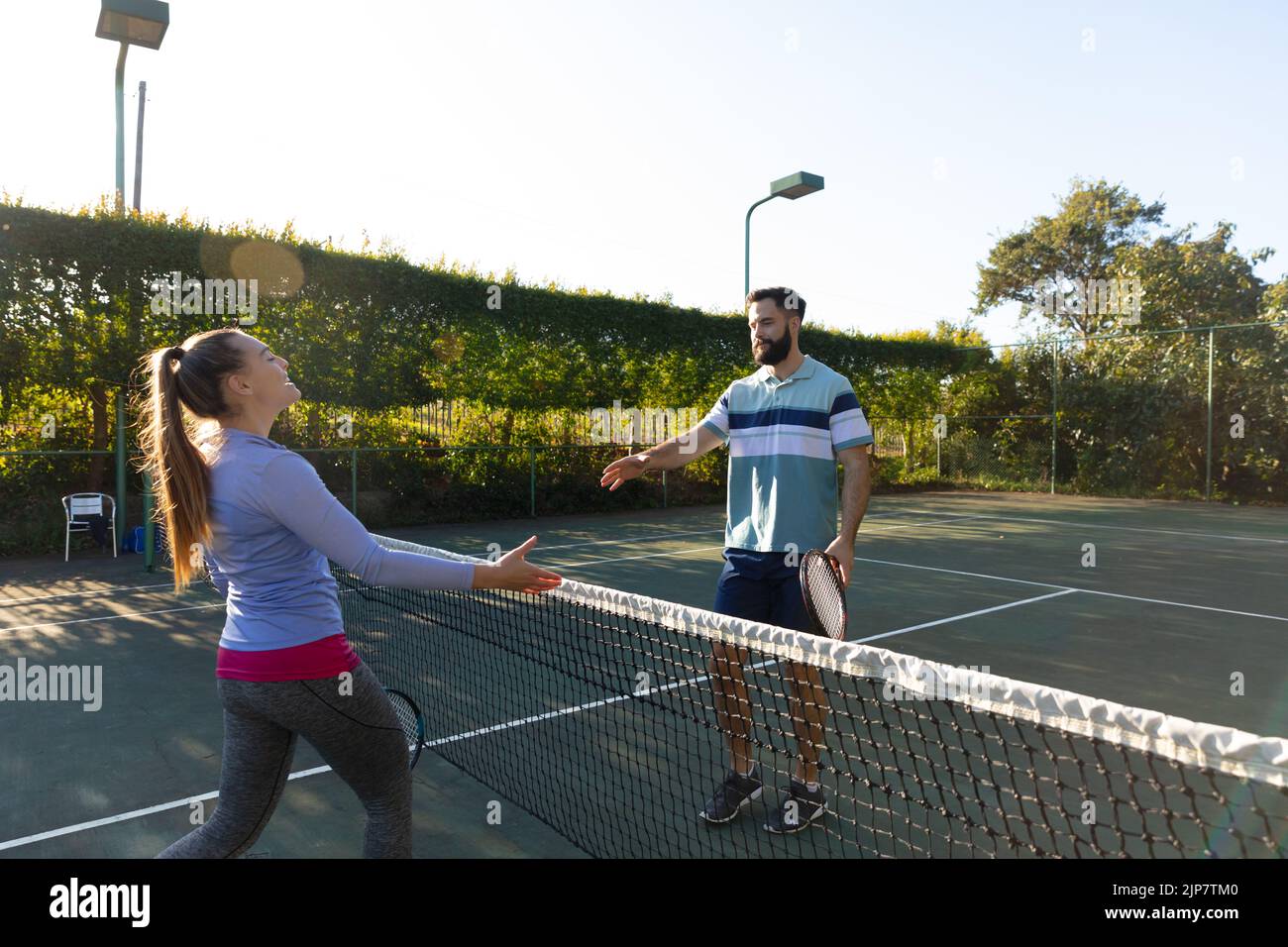 Happy caucasian couple playing tennis shaking hands over the net on
