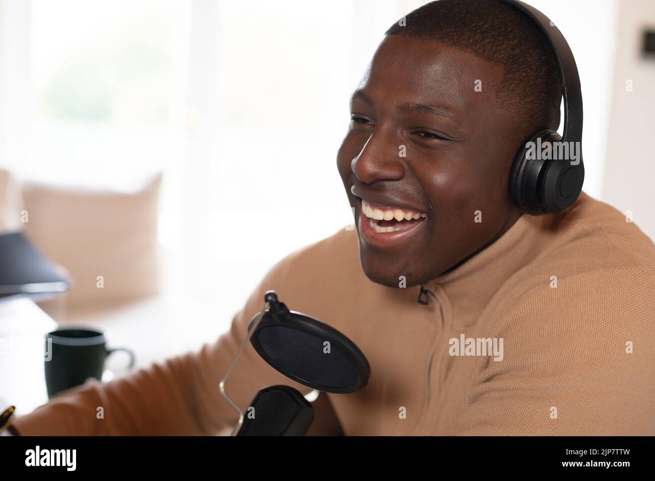 Laughing african american man making podcast at home wearing headphones Stock Photo