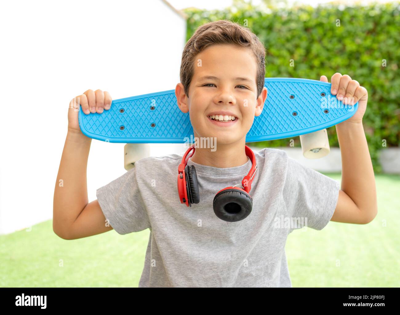 Happy boy carrying his skateboard on his back in the garden of his