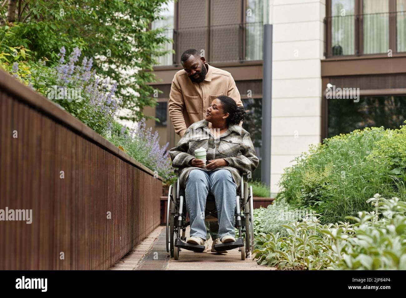 Full length portrait of black couple with young woman in wheelchair enjoying walk in city garden and looking at each other, copy space Stock Photo
