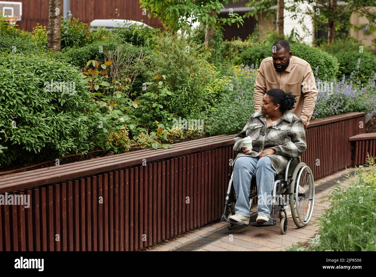 Full length portrait of black adult couple with partner in wheelchair enjoying walk together in city garden, copy space Stock Photo