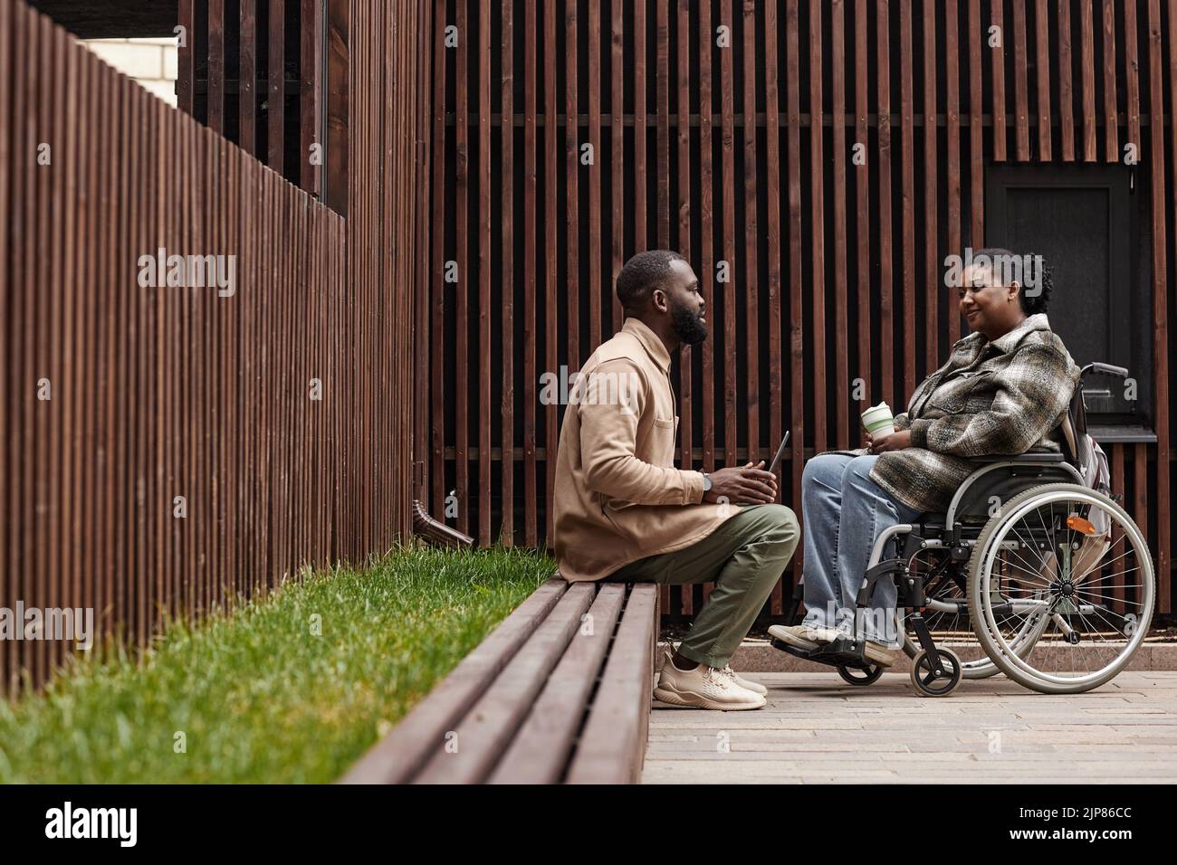 Graphic side view shot of young woman in wheelchair talking to friend ...
