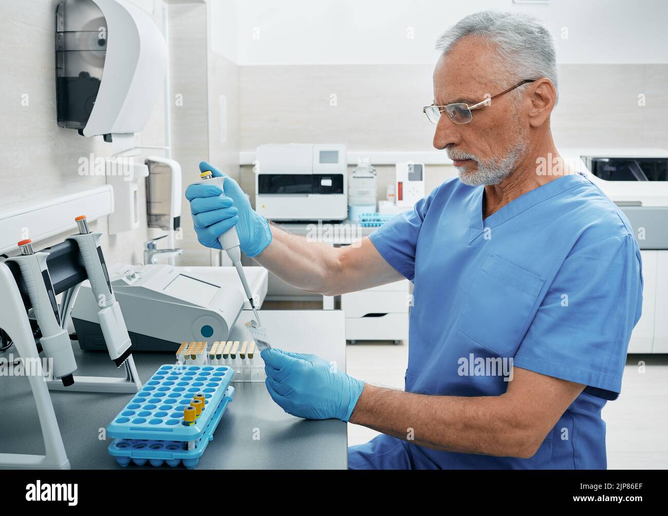 Mature male scientist with micropipette for test analyzes working at medical research laboratory. Laboratory technician determines person's blood type Stock Photo