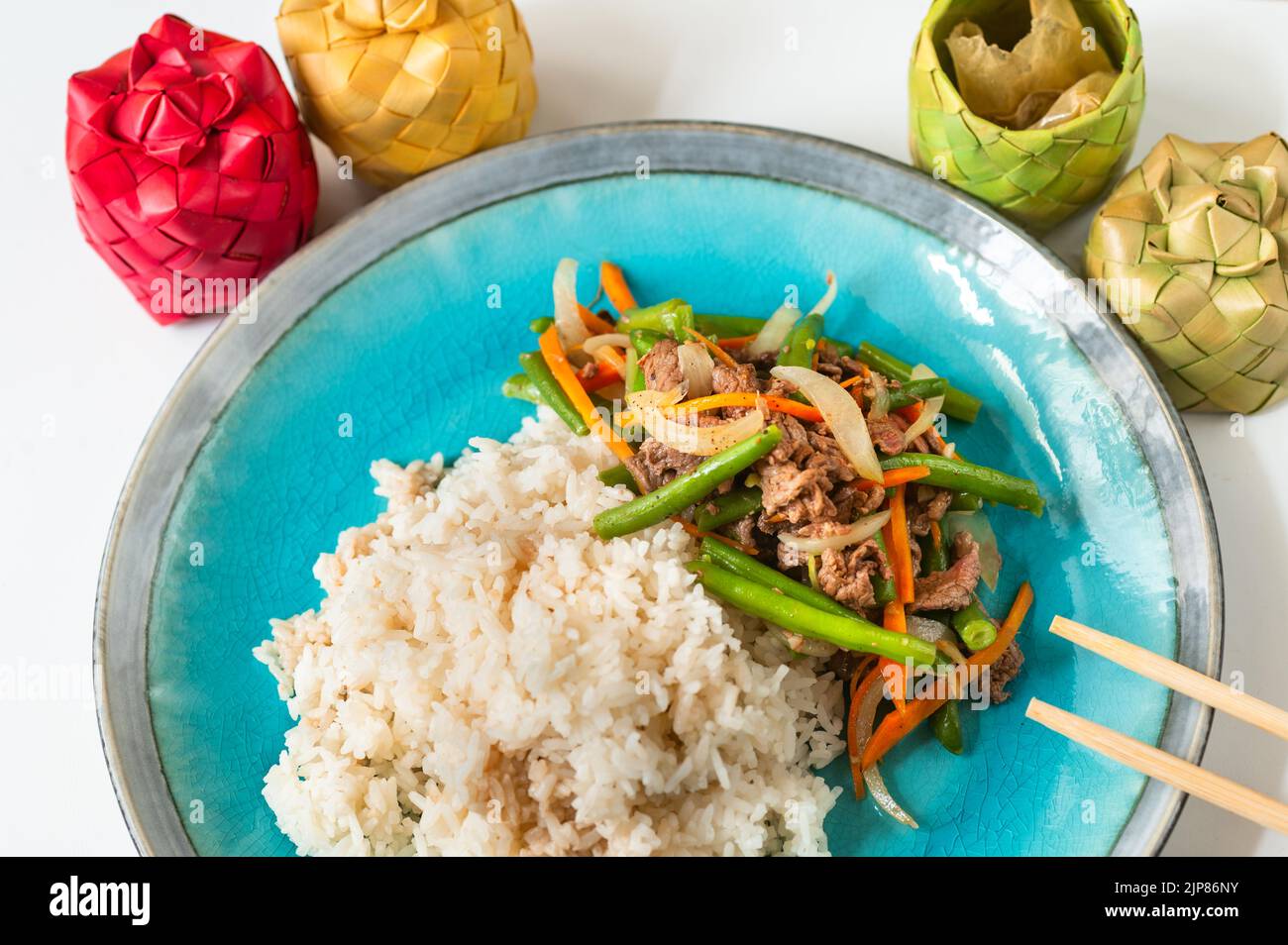 Asian (Vietnamese) food, stewed rice and fried beef, onion,green bean and carrot on blue plate, chopstick and 4 small bamboo box with condiment on whi Stock Photo