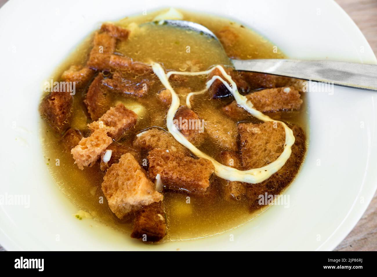 Garlic soup with sliced fried bread and melted cheese, spoon in white plate, closeup. Traditional Czech republic cuisine. Stock Photo