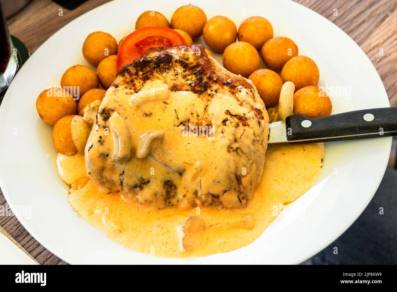 Pork steak with mushroom (chanterelle) creamy sauce, fried croquet, knife on white plate, closeup. Stock Photo