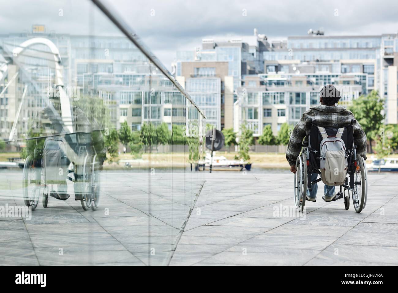 Back view of black woman in wheelchair outdoors with city skyline in background, copy space Stock Photo