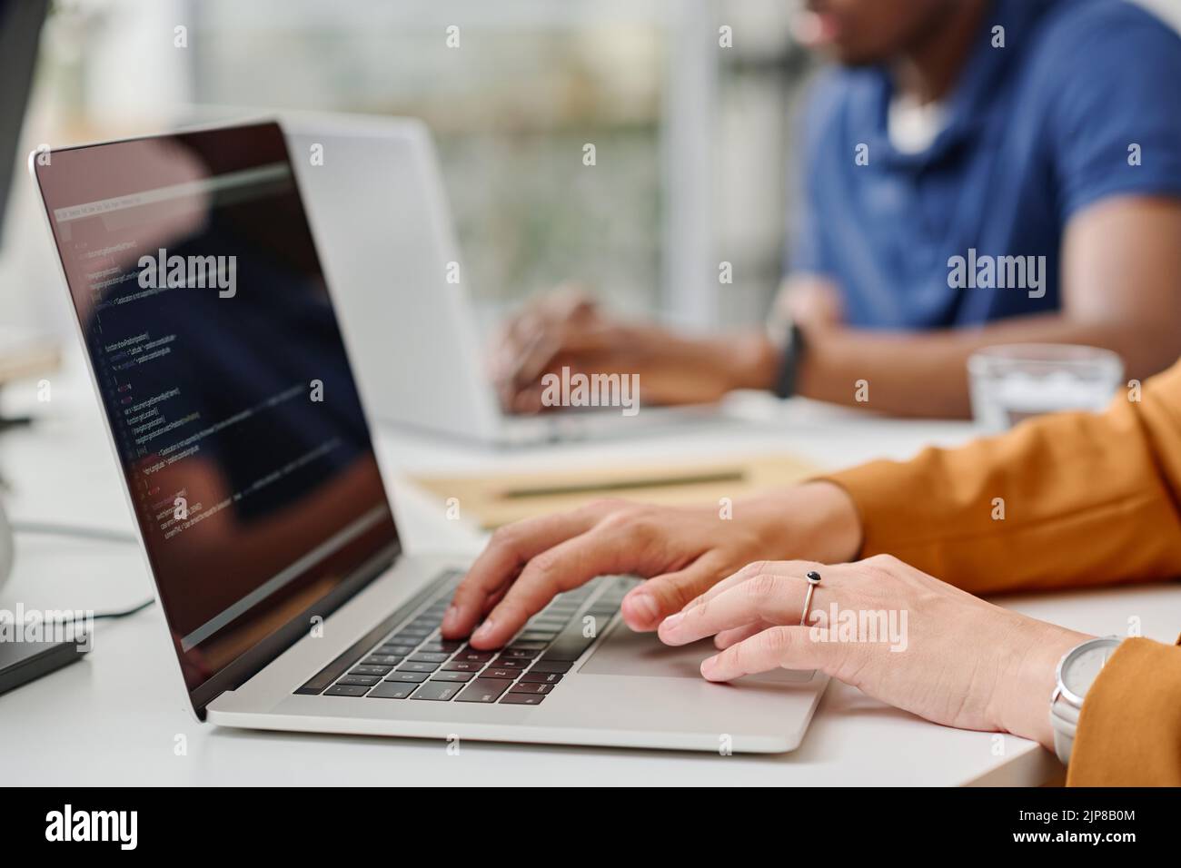 Close -up of female programmer typing codes on laptop during her work at office with colleagues Stock Photo