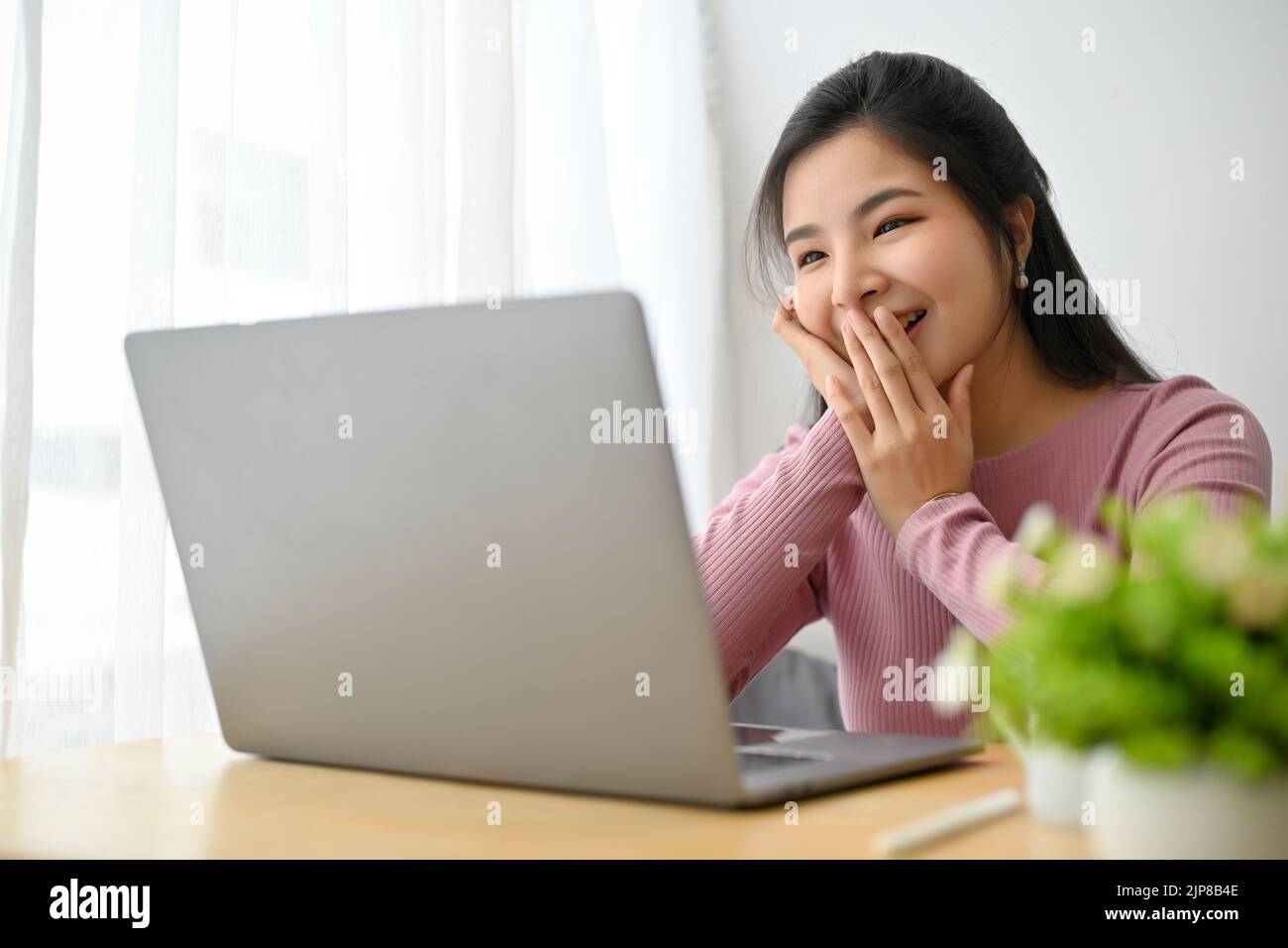 Pretty and cheerful young Asian female having a video call with her ...