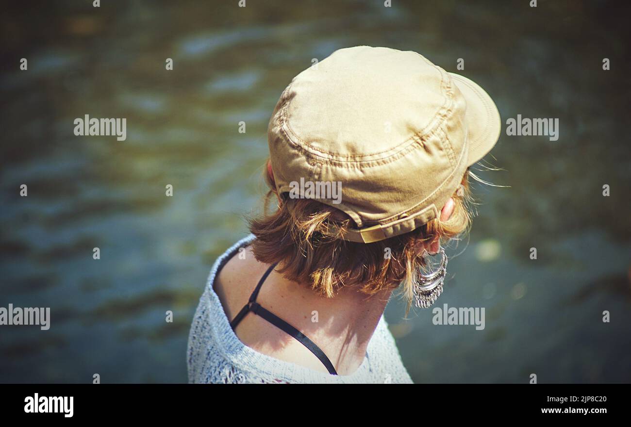 A closeup shot of a female's head from behind wearing a hat and looking toward the pond Stock Photo
