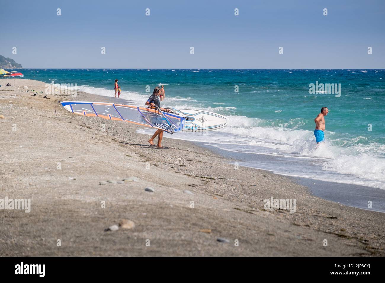 Windsurfer carrying his windsurfing board into the sea at Agiokmapos beach, Greece Stock Photo