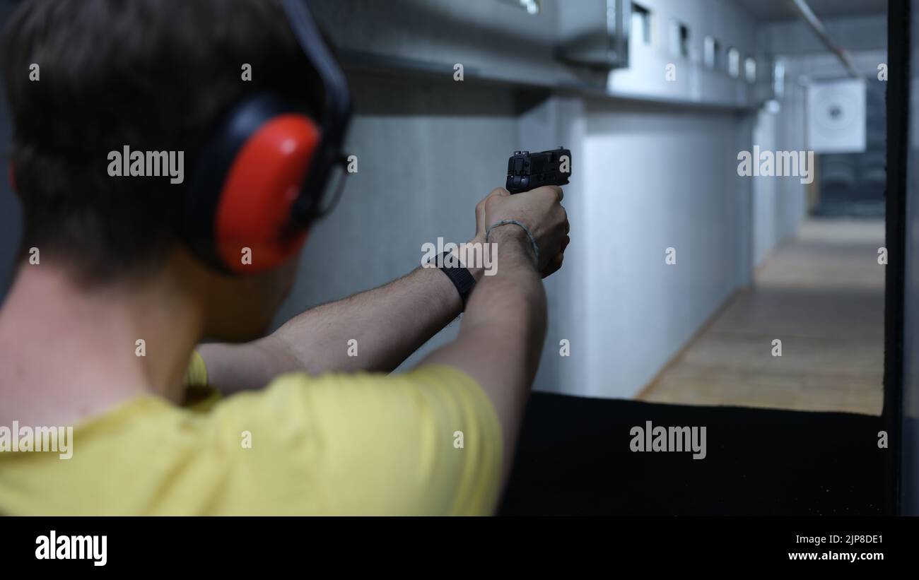Male shooter in headphones aiming pistol at target in shooting range