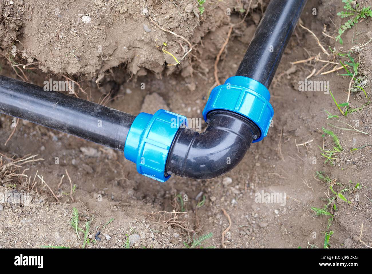 Elbow fitting and black pvc pipes at bend in trench outdoors Stock