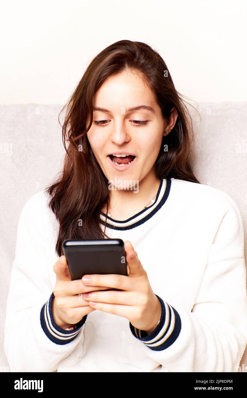 Happy millennial generation Hispanic Latina woman looking at cell phone screen, feeling excited reading a message, internet success Stock Photo