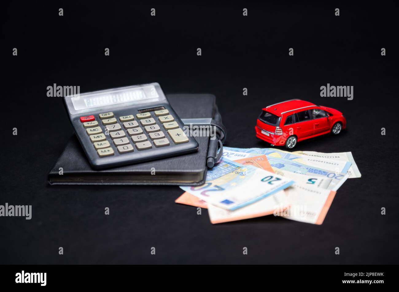 euro banknotes, calculator, notebook and red toy car on black