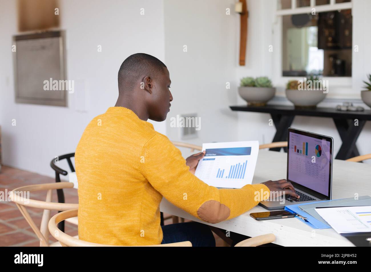 Side view of african american man using laptop nd looking at spreadsheets sitting at table at home Stock Photo