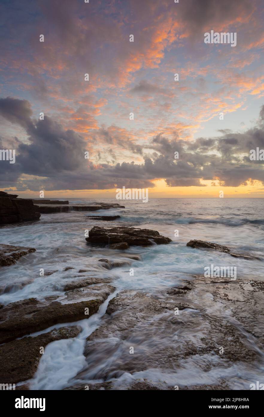 Sunrise over rocky ocean seascape with incredible clouds display some highlighting the sunrise colours, and water flow over rocks and in crevices Stock Photo
