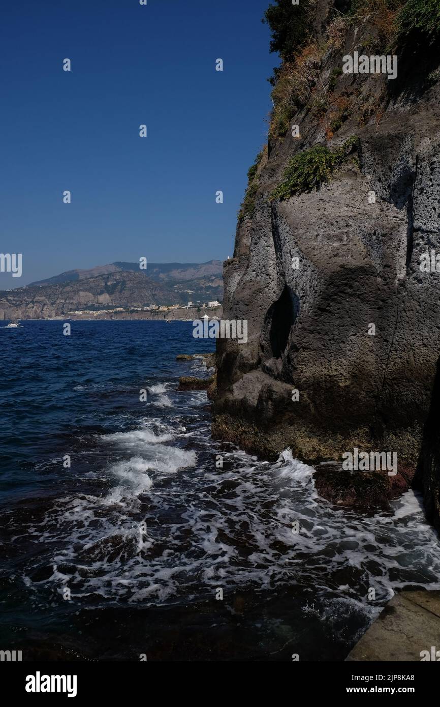 Close-up view of rock edge of Sorrento peninsular cliff  that meets the sea with a seagull nesting with the harbour and gulf of Naples in background Stock Photo