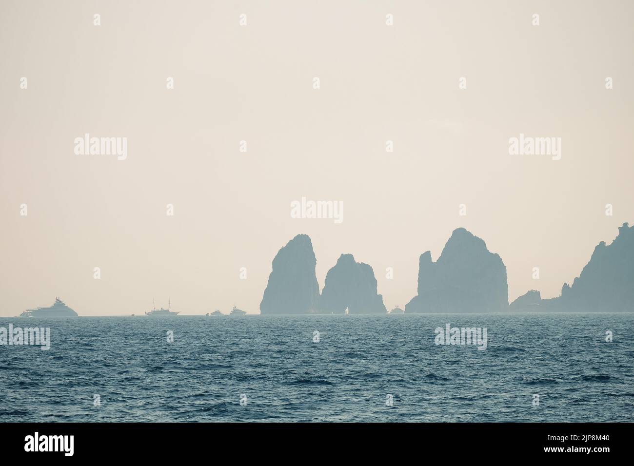 Capri faraglioni Wave erosion rock formations seascape of the island of Capri Italy in the bay of Naples seen in the sea mist with pleasure boats. Stock Photo