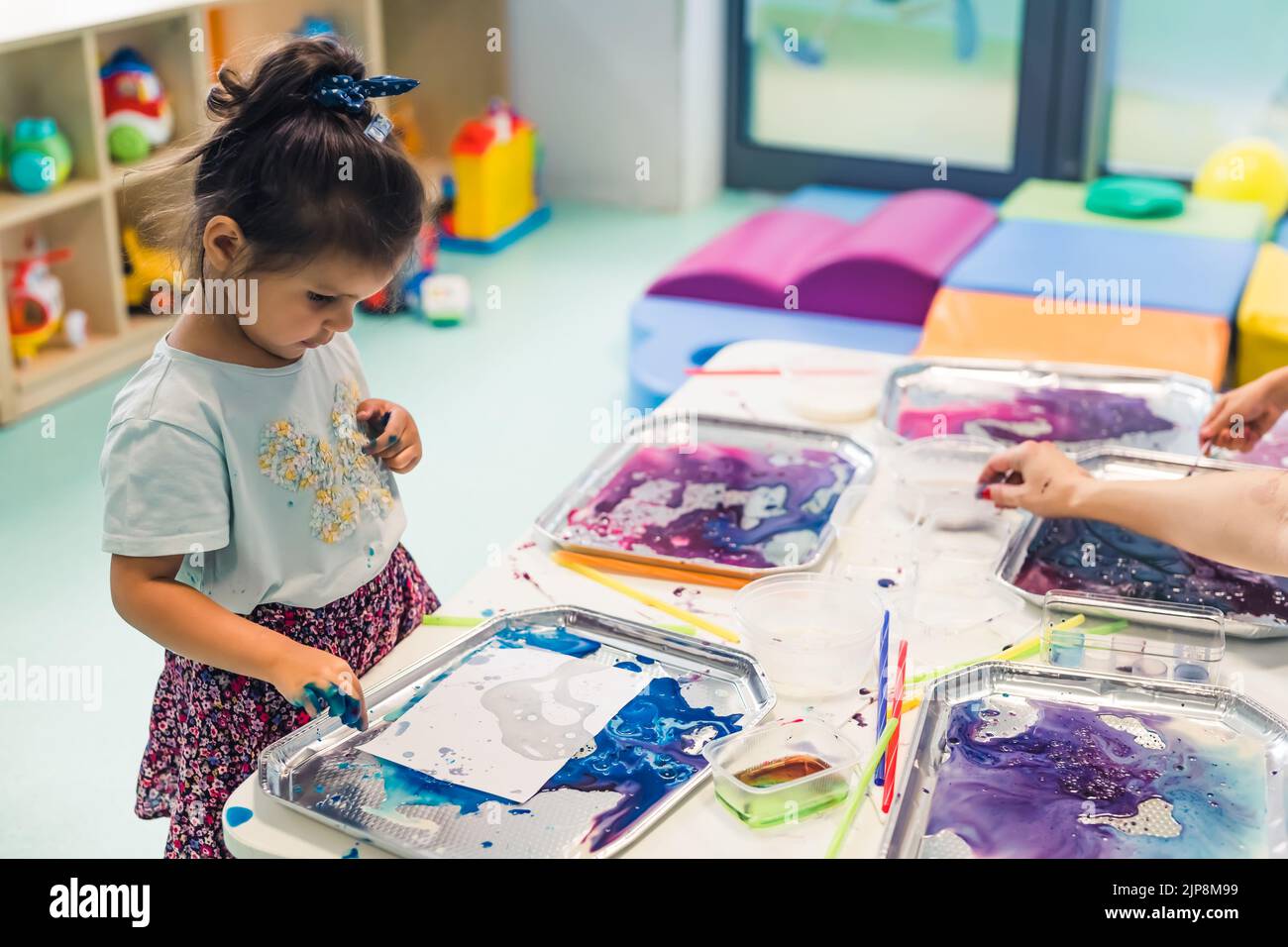 Multicultural group of children at the nursery school. Ethnic little girl milk painting, using pigments for color. Finger paint. High quality photo Stock Photo