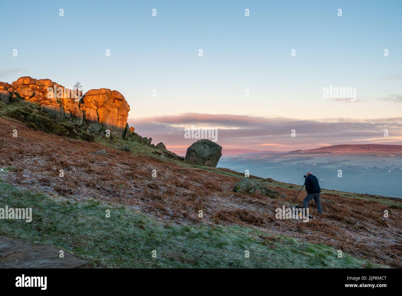 Photographer taking photos with a camera and tripod photographing sunrise at the Cow and Calf Rocks, Ilkley Moor, England. Stock Photo