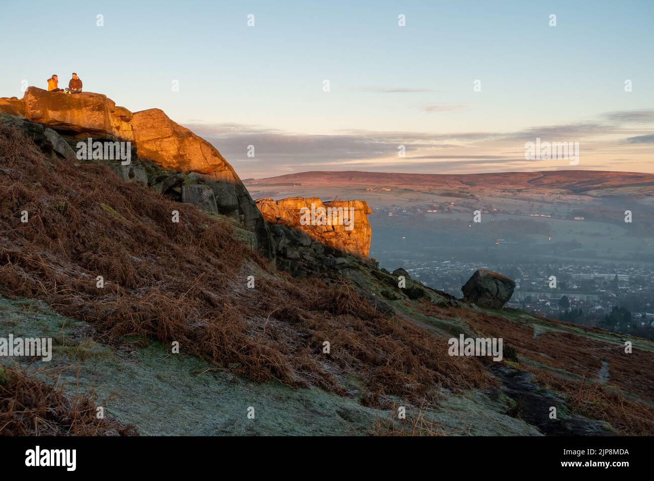 Couple enjoying a hot drink at sunrise at the Cow and Calf Rocks, Ilkley Moor, England. Stock Photo