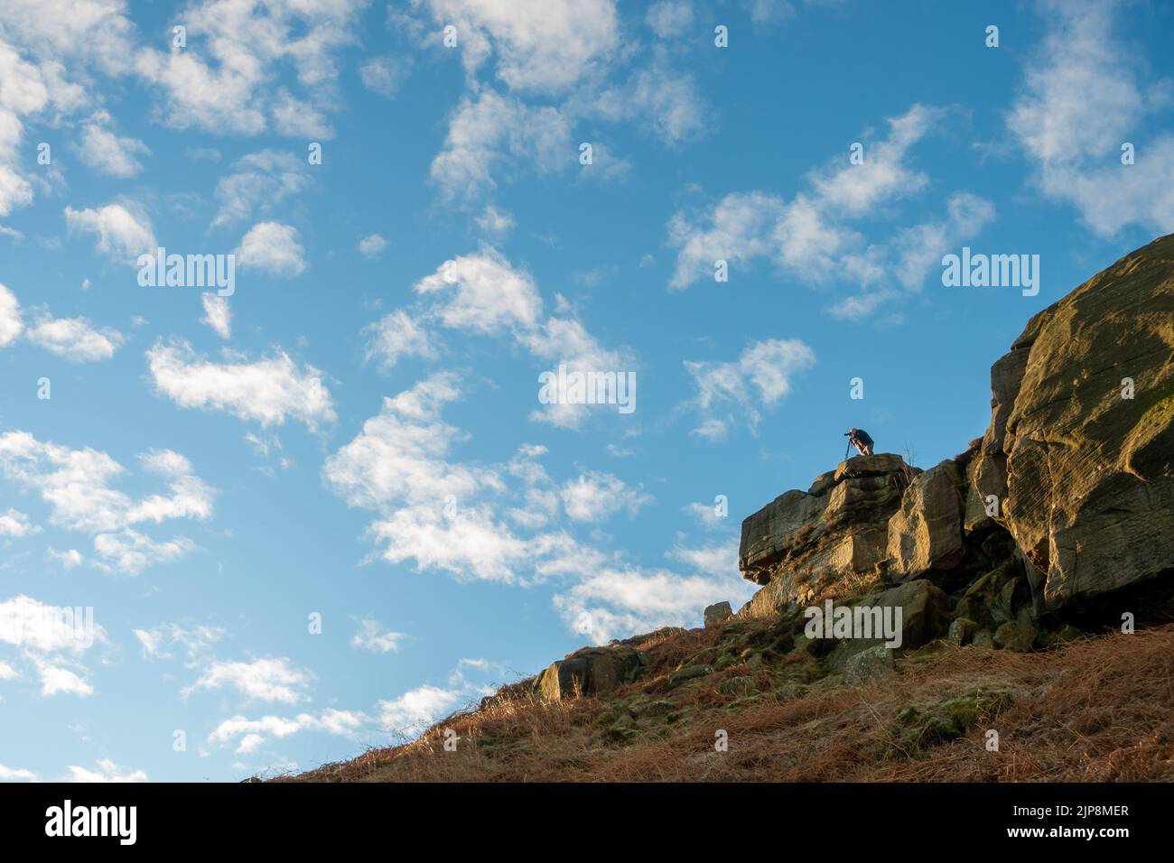 Photographer with tripod photographing sunrise from the Cow and Calf Rocks, Ilkley Moor, England. Stock Photo