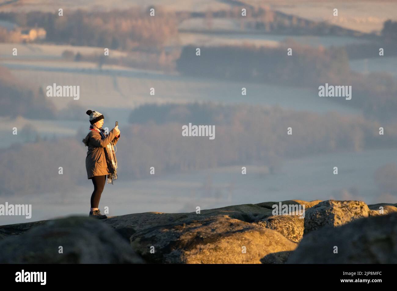 Woman in winter taking photos of the sunrise from Ilkley Moor. West Yorkshire, England Stock Photo