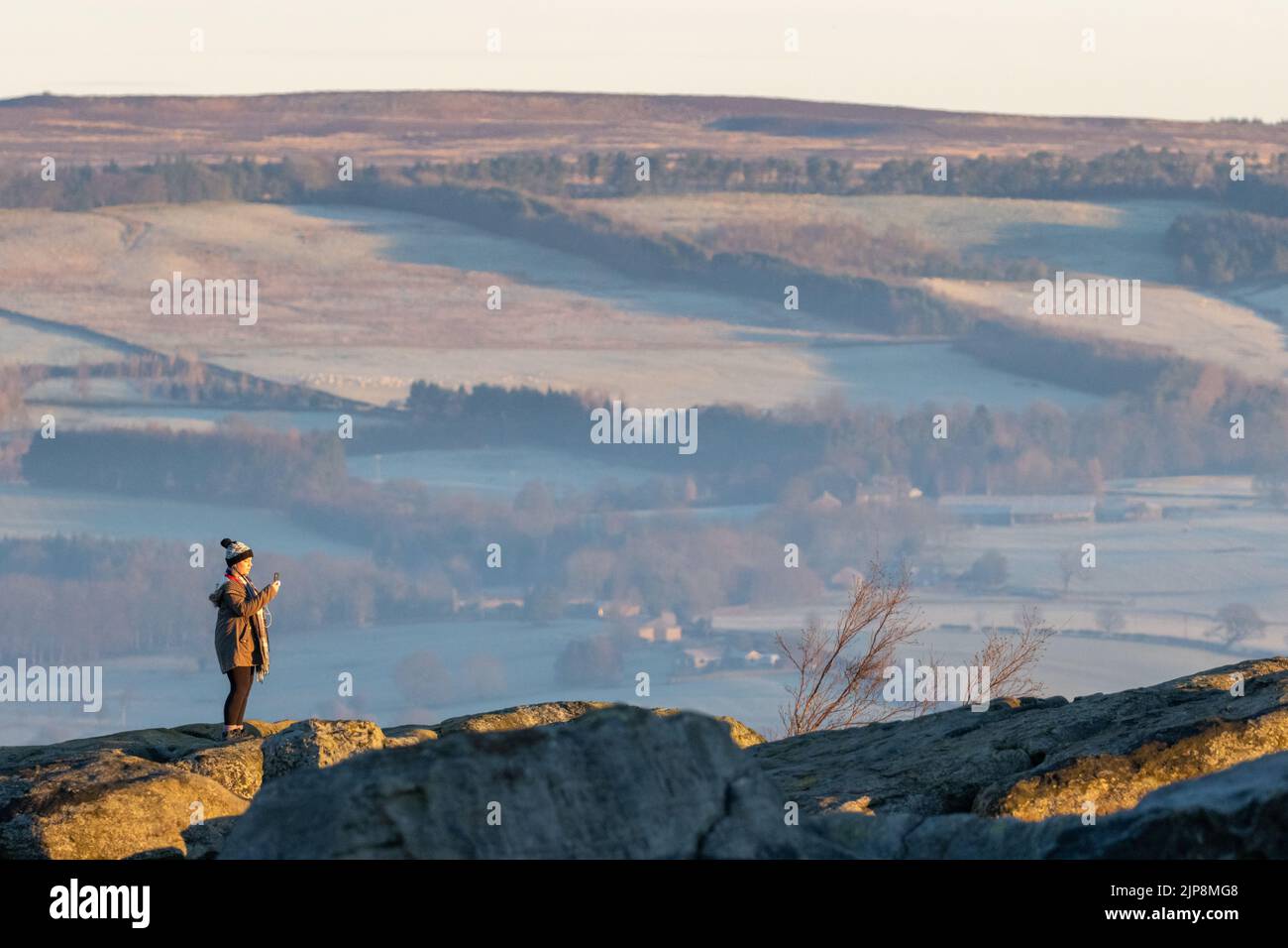 Woman in winter taking photos of the sunrise from Ilkley Moor. West Yorkshire, England Stock Photo