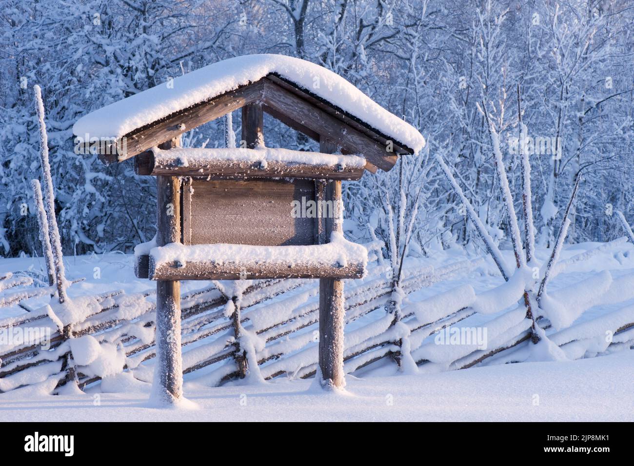 Snow covered empty information board and old fence in winter landscape. Stock Photo